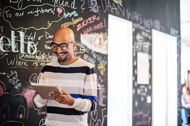 Smiling man using tablet in front of chalkboard wall.