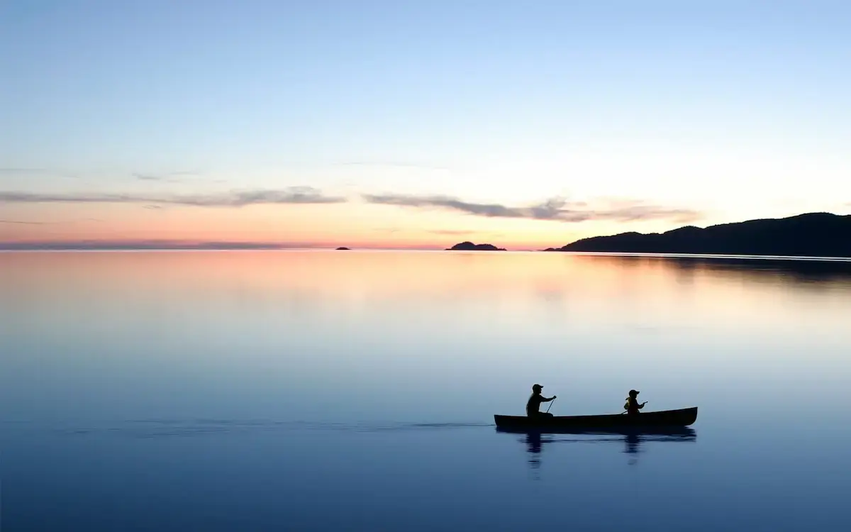 Silhouettes canoeing on a calm lake during a serene sunset.