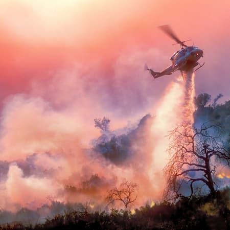A helicopter dropping water over a raging wildfire in a dry landscape, illustrating the effects of prolonged droughts and climate change on forest fires. A helicopter dropping water over a raging wildfire in a dry landscape, illustrating the effects of prolonged droughts and climate change on forest fires.