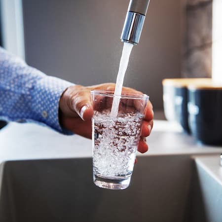 A person filling a glass with fresh tap water in a kitchen, representing clean drinking water accessibility and daily hydration.
