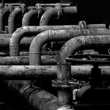 A series of old, corroded industrial water pipes with rust and grime, illustrating the challenges of aging water infrastructure and the need for maintenance.