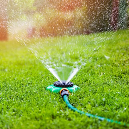 A garden sprinkler spraying water on a green lawn during a sunny day, representing water consumption for outdoor landscaping and irrigation efficiency.