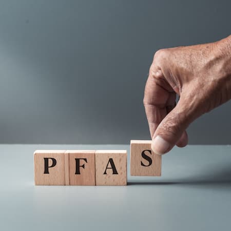 A hand placing a wooden block with the letters "PFAS," highlighting the issue of toxic chemical contamination in water and the environment. A hand placing a wooden block with the letters "PFAS," highlighting the issue of toxic chemical contamination in water and the environment.