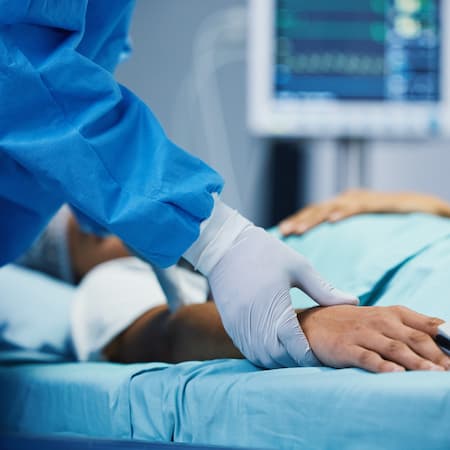 A healthcare professional wearing gloves checking a patient's pulse in a hospital bed, with medical monitors in the background, representing critical care and medical support. A healthcare professional wearing gloves checking a patient's pulse in a hospital bed, with medical monitors in the background, representing critical care and medical support.