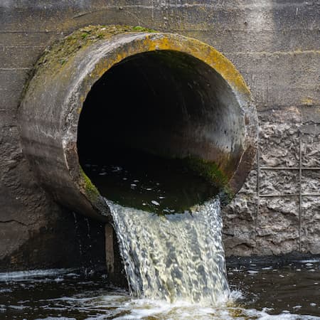 A large concrete pipe releasing untreated wastewater into a river, highlighting the environmental impact of water pollution and inadequate sewage treatment. A large concrete pipe releasing untreated wastewater into a river, highlighting the environmental impact of water pollution and inadequate sewage treatment.