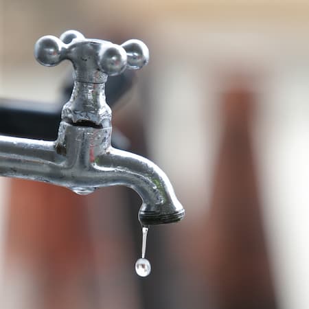 A close-up of an old metal faucet with a single droplet of water falling, emphasizing the importance of water conservation and leakage prevention. A close-up of an old metal faucet with a single droplet of water falling, emphasizing the importance of water conservation and leakage prevention.